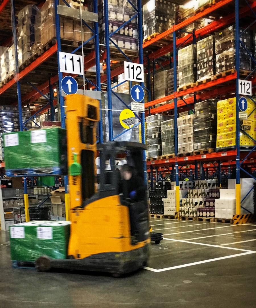 Forklift moving pallets down a numbered aisle in a distribution warehouse